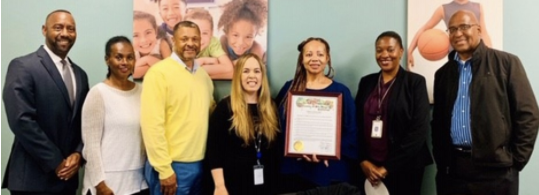 image of seven people, the woman to the right of center is holding a certificate.