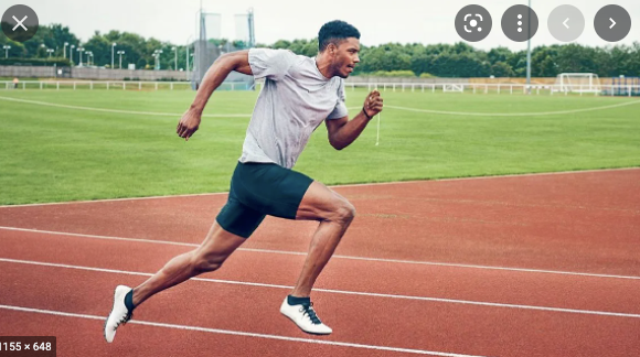 Runner mid stride on a track. There is grass and stadium equipment in the background.